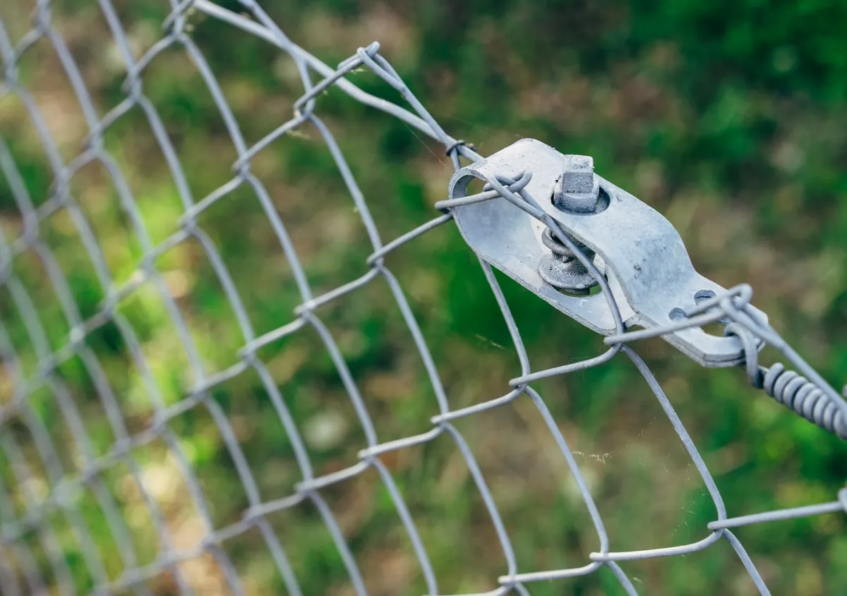 A galvanised wire mesh fence with a steel tensioner